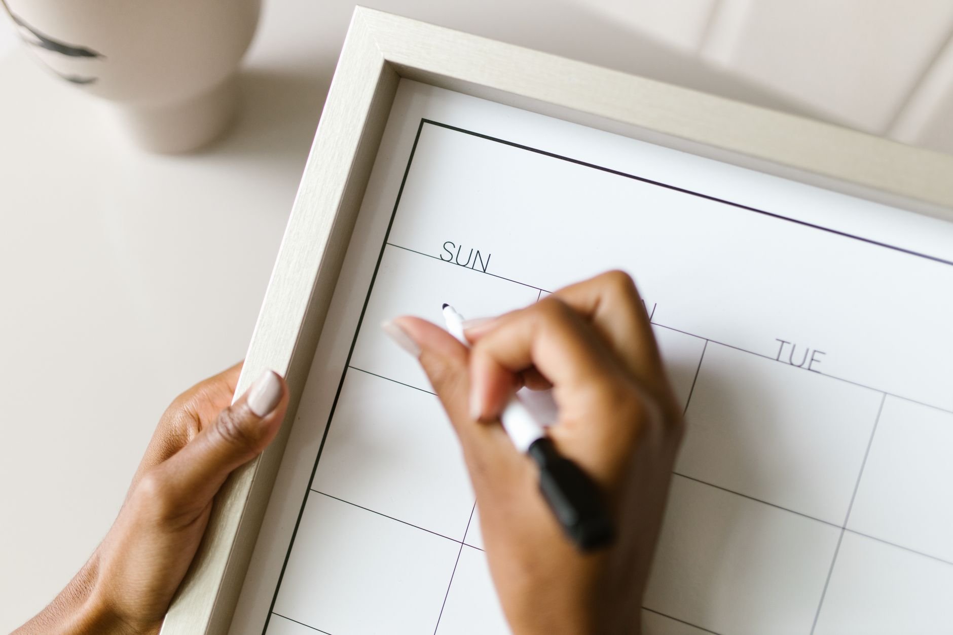 Hands holding a wall calendar, writing with a marker, organizing schedule